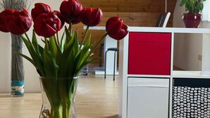 Una sala de estar moderna con techo de madera, un jarrón de vidrio con tulipanes rojos sobre una mesa de vidrio, y un mueble blanco con cajones rojos.
