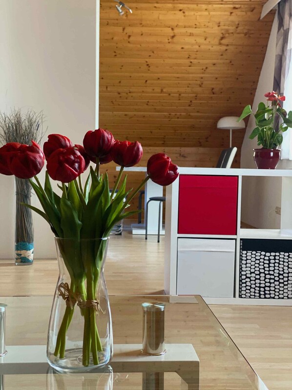 A modern living room with a wooden ceiling, a glass vase with red tulips on a glass table, and a white cabinet with red drawers.