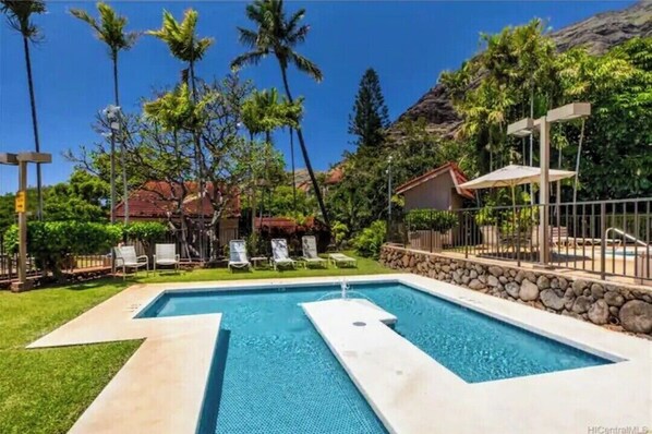 A swimming pool with lounge chairs, surrounded by palm trees and a stone wall.