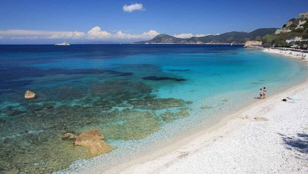 Una playa con agua turquesa cristalina, arena blanca y afloramientos rocosos.
