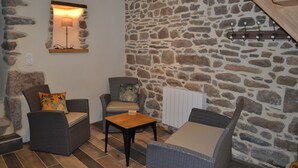 A cozy room with stone walls, wicker furniture, and a small table. - La Maison de Félicie (Saint-Pol-de-Léon)