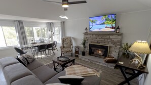 Un salon comprenant un canapé, une cheminée, un téléviseur et un coin repas avec des chaises et une table.