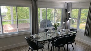 Un espace repas avec une table en verre, des chaises noires et une vue sur la verdure environnante.