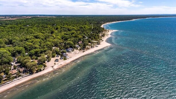 Vue aérienne d’une zone côtière avec une plage, une forêt dense et des eaux d’un bleu limpide.
