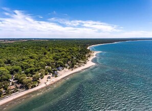 Vista aérea de una zona costera con playa, bosque denso y aguas azules cristalinas.