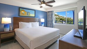 Habitación de hotel con una cama grande, dos mesitas de noche con lámparas, un ventilador de techo, un ventanal con vistas y un escritorio con una computadora portátil.