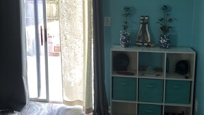 A room with teal walls, a wooden floor, a sliding glass door with grey curtains, and a white shelving unit with decorative items. - Peaceful, close to water attractions & Fishing (Panama City)