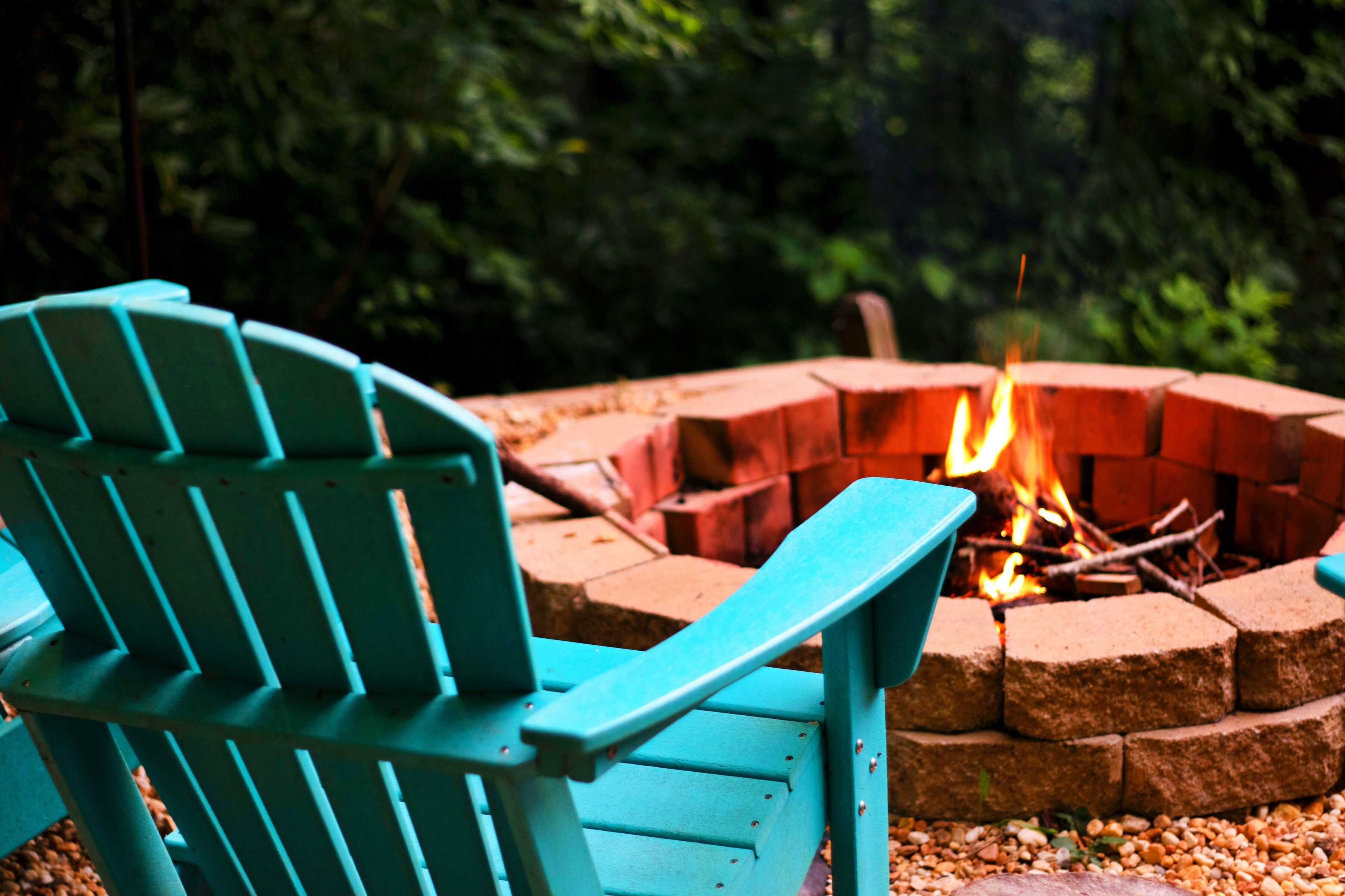 A teal Adirondack chair near a fire pit with logs.