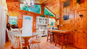 A wooden cabin interior with a dining area, kitchen, and a large wooden door. - Cozy Cabin Retreat - Hot Tub, Fireplace & Fire Pit - Minutes from Blue Ridge (Blue Ridge)