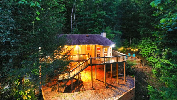 A wooden cabin with a deck and stairs, surrounded by dense forest. - Cozy Cabin Retreat - Hot Tub, Fireplace & Fire Pit - Minutes from Blue Ridge (Blue Ridge)