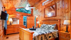 A wooden cabin bedroom with a bed, nightstands, a TV, and a ceiling fan. - Cozy Cabin Retreat - Hot Tub, Fireplace & Fire Pit - Minutes from Blue Ridge (Blue Ridge)