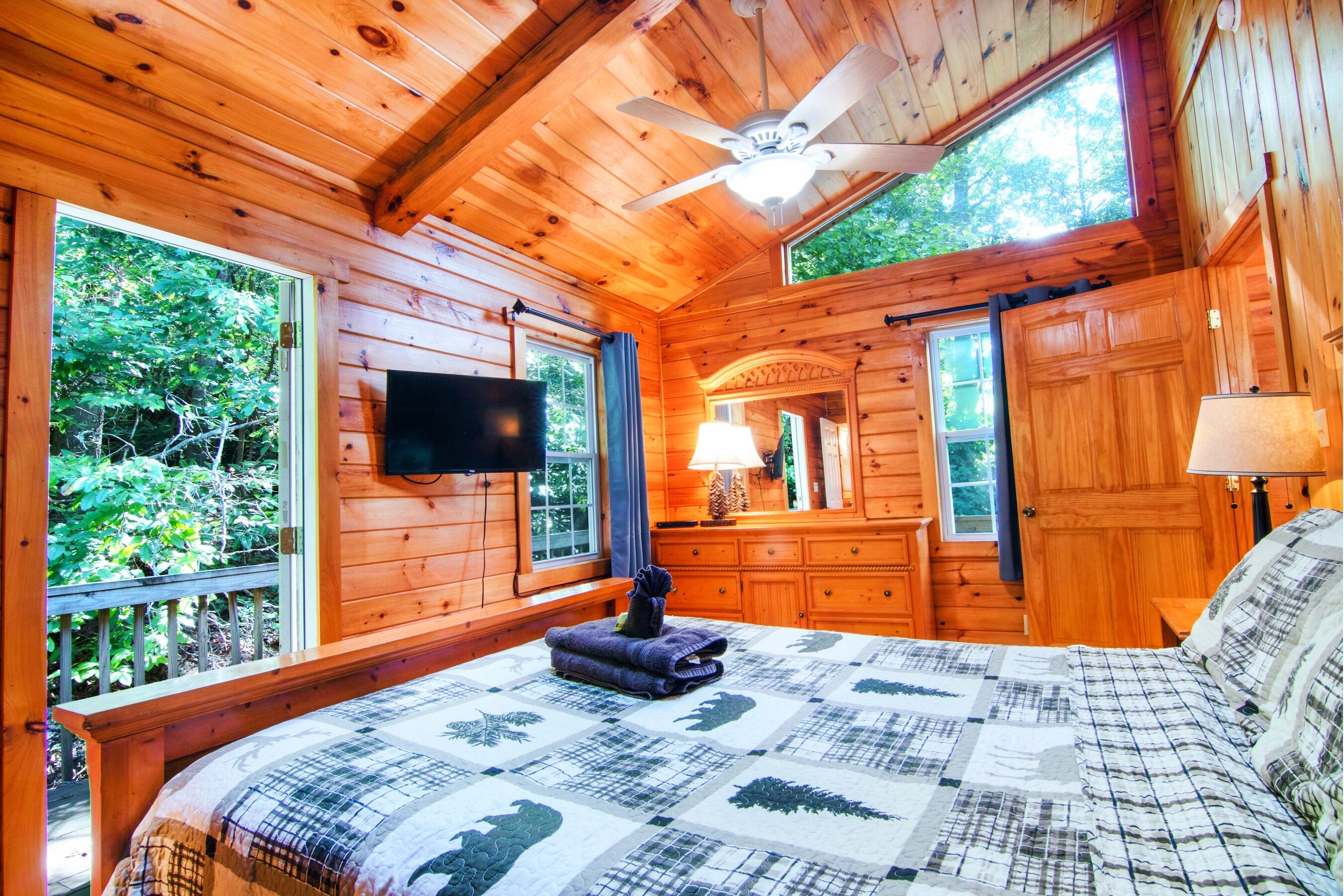 Une chambre dans un chalet en bois, avec un lit, un ventilateur de plafond, une télévision et une commode.