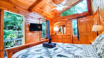 Une chambre dans un chalet en bois, avec un lit, un ventilateur de plafond, une télévision et une commode.