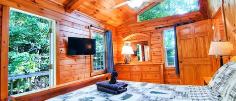 A wooden cabin bedroom with a bed, a ceiling fan, a TV, and a dresser.