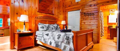 A wooden cabin bedroom with a bed, two bedside tables, a nightstand, and a dresser.