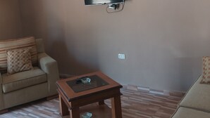 Ett vardagsrum med en platt-TV som är monterad på väggen, en takfläkt och ett soffbord i trä med en glasskål.