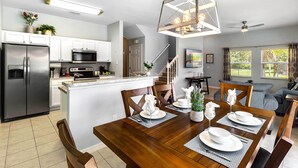A modern kitchen with white cabinets, stainless steel appliances, and a dining area with a wooden table set for four. - Bay Lilly Family Villa Close to Parks sleeps 8 (Kissimmee)