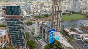Um edifício alto com design moderno, cercado por um horizonte urbano e um corpo de água.