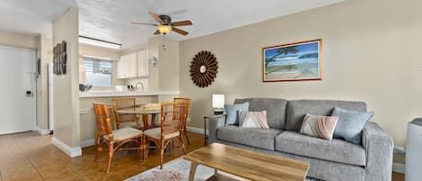 Ein Wohnzimmer mit grauem Sofa, Couchtisch aus Holz und einem Essbereich mit Korbstühlen.