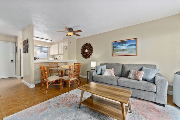 A living room with a grey sofa, wooden coffee table, and a dining area with wicker chairs.
