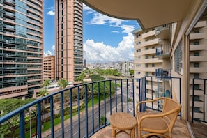 A balcony with wicker furniture overlooking a cityscape with modern buildings and a clear sky.