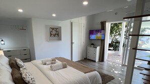 Ein modernes Schlafzimmer mit einem großen Bett, Nachttischen, einem Fernseher und Blick ins Freie.