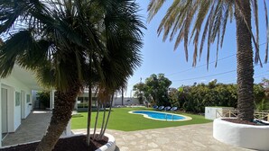 Ein Poolbereich mit blauem Himmel, Palmen und einem gepflegten Rasen.