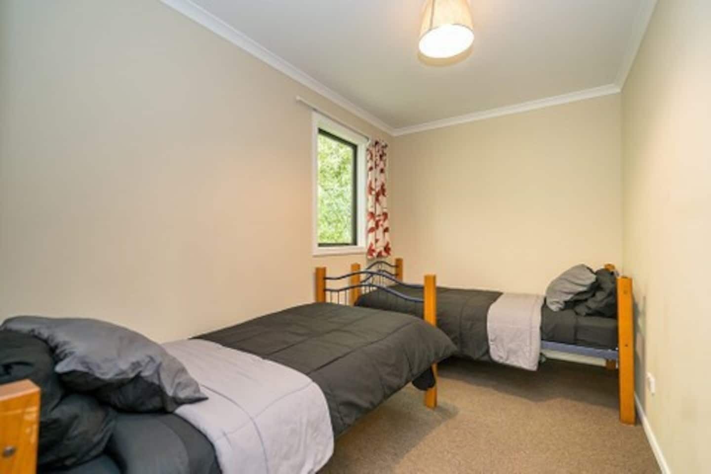 Un petit logement composé d’une seule pièce, comprenant deux lits simples, une fenêtre avec des rideaux et un luminaire au plafond.