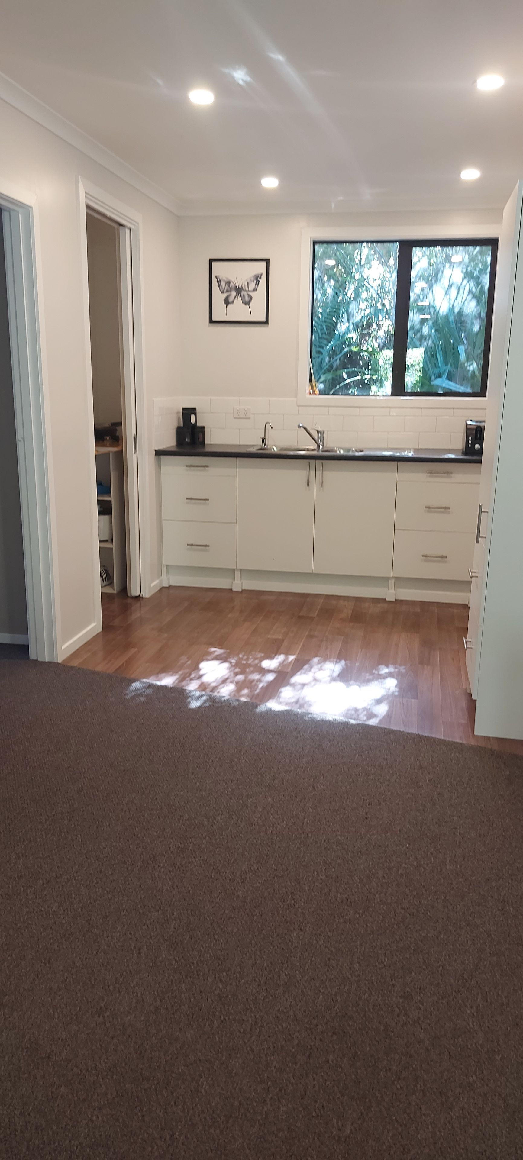 A kitchen with white cabinets, a window, and a butterfly artwork.