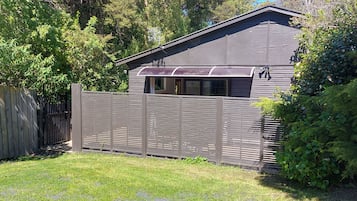Une cour arrière clôturée, avec une terrasse en bois, un petit abri de jardin et un feuillage dense.