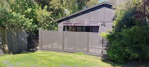 A fenced backyard with a wooden deck, a small shed, and dense foliage. - The Sleepout - Your little house away from home! (Dunedin)
