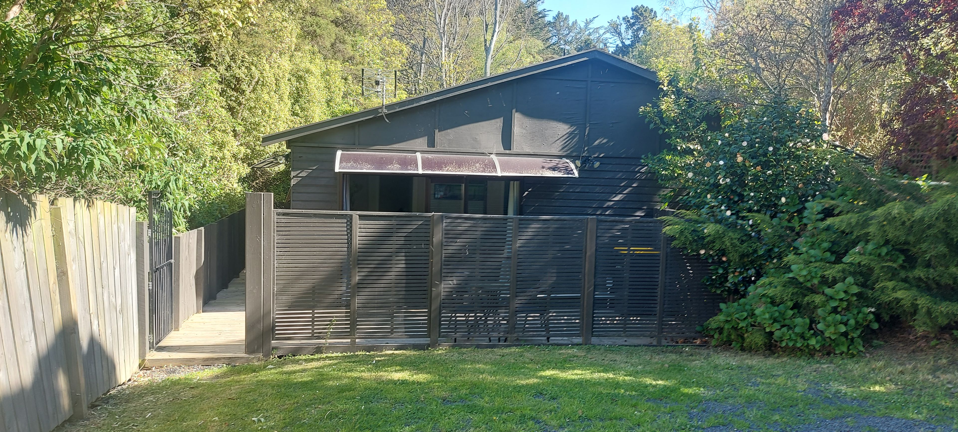 A small, dark-colored building with a sloped roof, a wooden fence, and a metal gate.