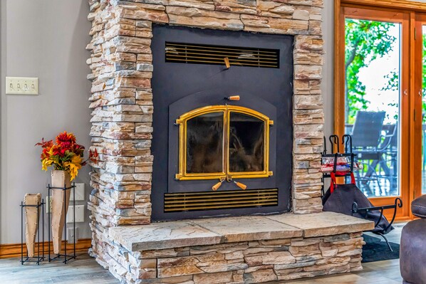 Una chimenea de piedra con puerta de cristal, una mesita con un florero y una silla frente a la puerta.