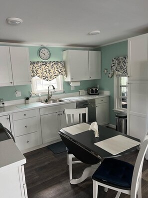 A compact kitchen with white cabinets, a black dining table, and a clock on the wall. - Cool Breeze near the sea! Perfect for a family of 4! (Surfside Beach)