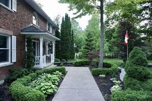 Ein Ziegelhaus mit Veranda, einer Flagge und einem gepflegten Garten mit verschiedenen Pflanzen und einem Weg.