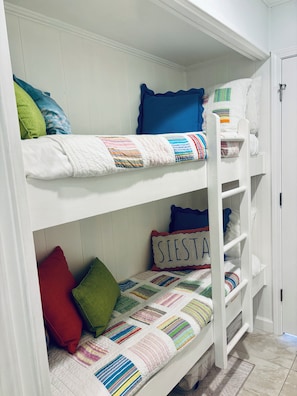 A bunk bed with a quilted bedspread and pillows, a ladder, and a door to a room.