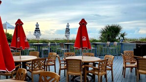 Eine Terrasse mit Sitzgelegenheiten im Freien, roten Coca-Cola Sonnenschirmen und Blick auf den Strand.