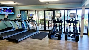 Ein Fitnessraum mit Laufbändern, Crosstrainern und einem Fernsehbildschirm, der ein Sportereignis zeigt.
