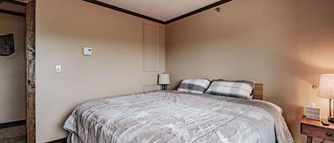 Una habitación de hotel con una cama grande, una mesita de noche con lámpara, y una puerta que da a otra habitación.