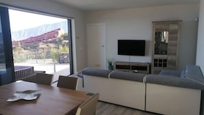 A modern living room with a wooden dining table, grey sofa, and a flat-screen TV mounted on the wall. - VILLA "LA FLORIDA" - WONDERFUL VIEWS - POOL - WIFI (CN)