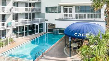 A swimming pool with a blue umbrella labeled "CAFE" and a multi-story building with balconies.