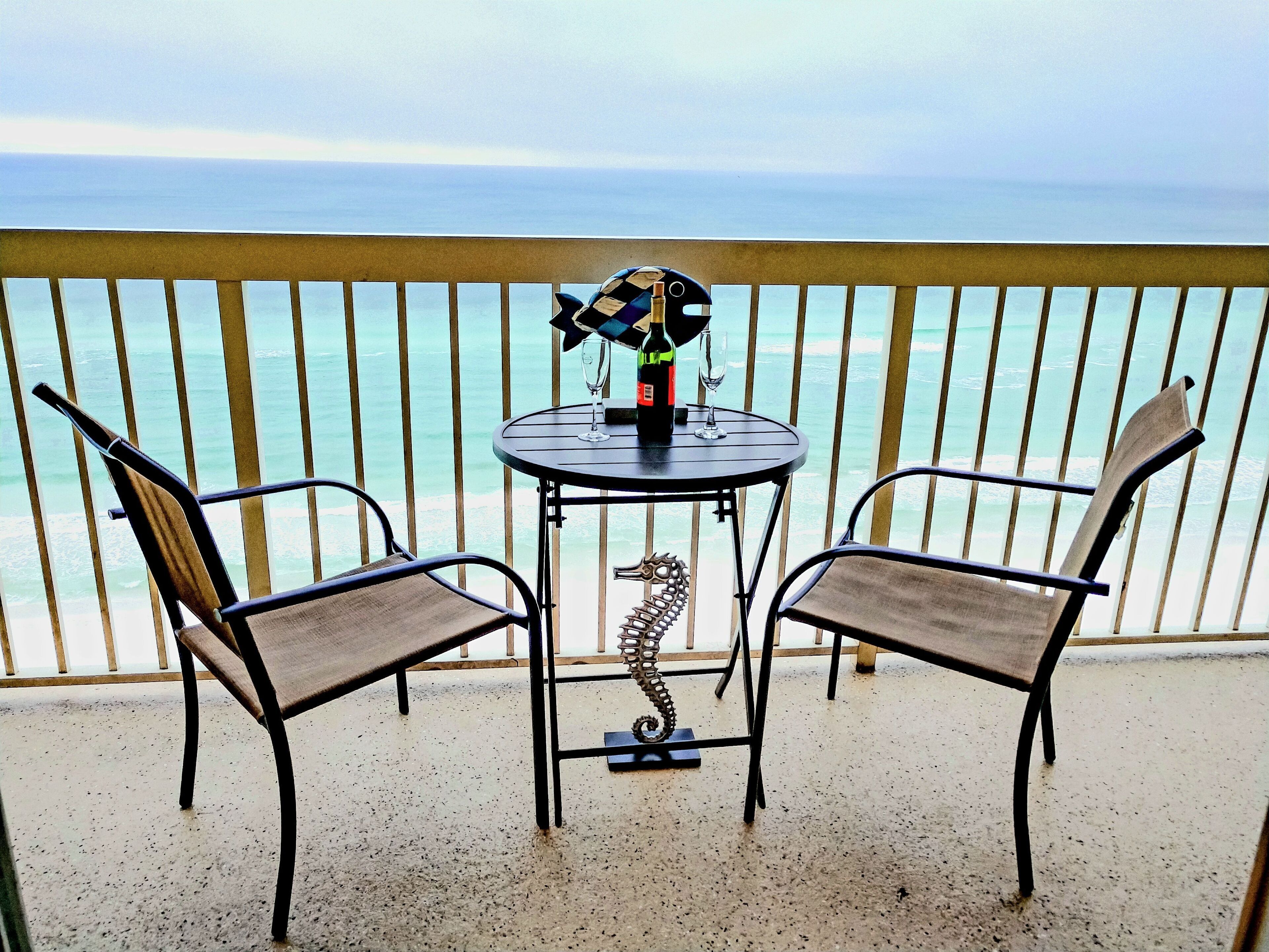 A balcony with a table and two chairs, overlooking the sea.
