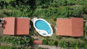 An aerial view of a property with a swimming pool surrounded by a fence, two red-roofed buildings, and lush greenery. - Indigo Palomino Beautiful House (Palomino)