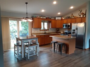 A modern kitchen with wooden cabinets, a stainless steel refrigerator, a microwave, and a large island with stools.