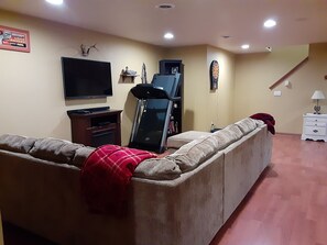 A living room with a sofa, a flat-screen TV, a gaming console, and a dartboard.