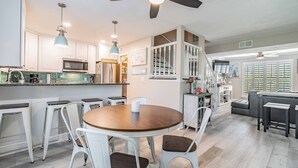 Une cuisine moderne avec des meubles blancs, un îlot central et un coin repas comprenant une table ronde et des chaises blanches.