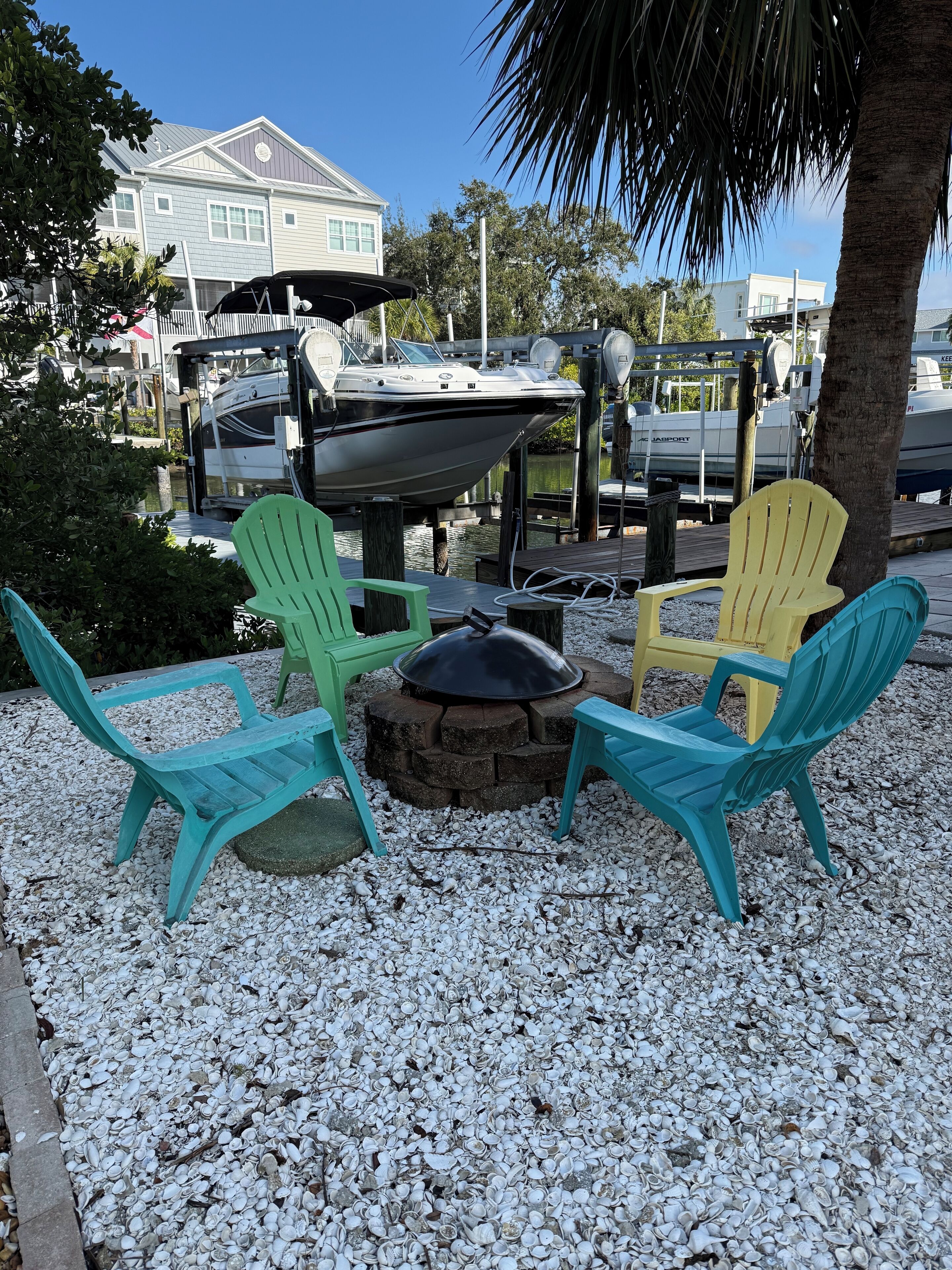 Un patio con dos sillas Adirondack, un hogar para fuego y un muelle con barcos.