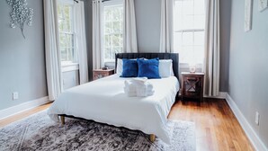 Een slaapkamer met een bed, twee nachtkastjes, een raam en een decoratie aan de muur.