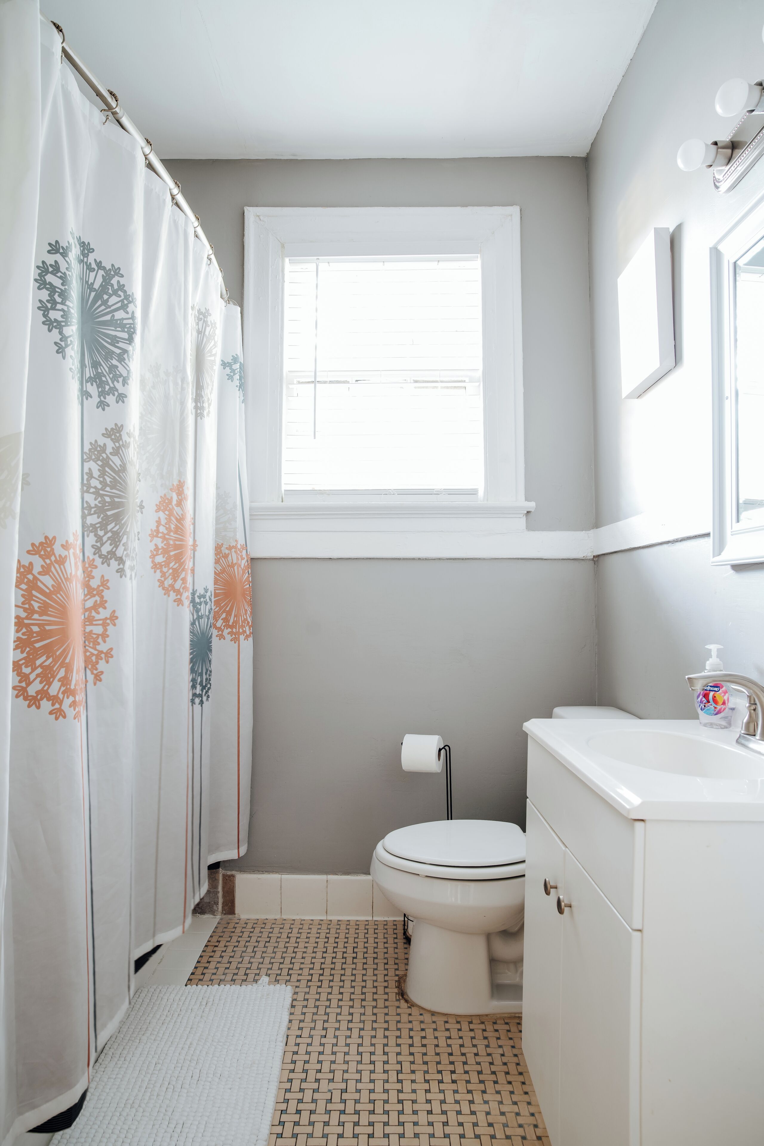 A bathroom with a toilet, a sink, a window, and a shower curtain with a floral pattern.