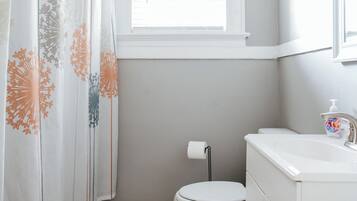 A bathroom with a toilet, a sink, a window, and a shower curtain with a floral pattern.